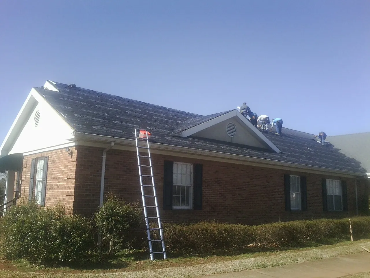 Crew tearing shingles off a brick ranch roof with a ladder set — Emergency Roof Repair work by our crew in Johnson