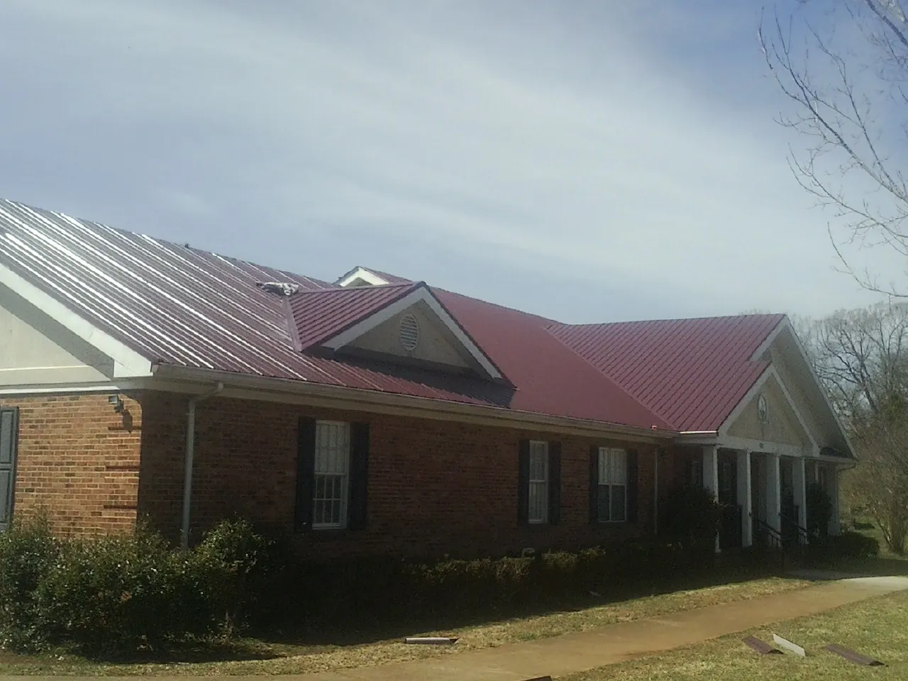 Red metal roof with gabled entries on a long brick building, from a Hail Damage Roof Repair job in Johnson