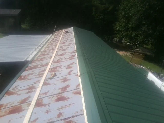 Old rusted panels beside newly installed green metal roofing — Wind Damage Roof Repair by Roofing Brothers in Johnson