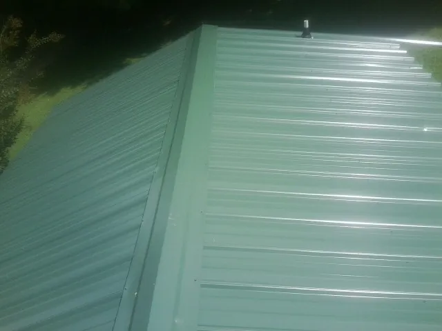 New green metal panels meeting at the ridge of a roof — Flat Roof Repair work by our crew in Johnson