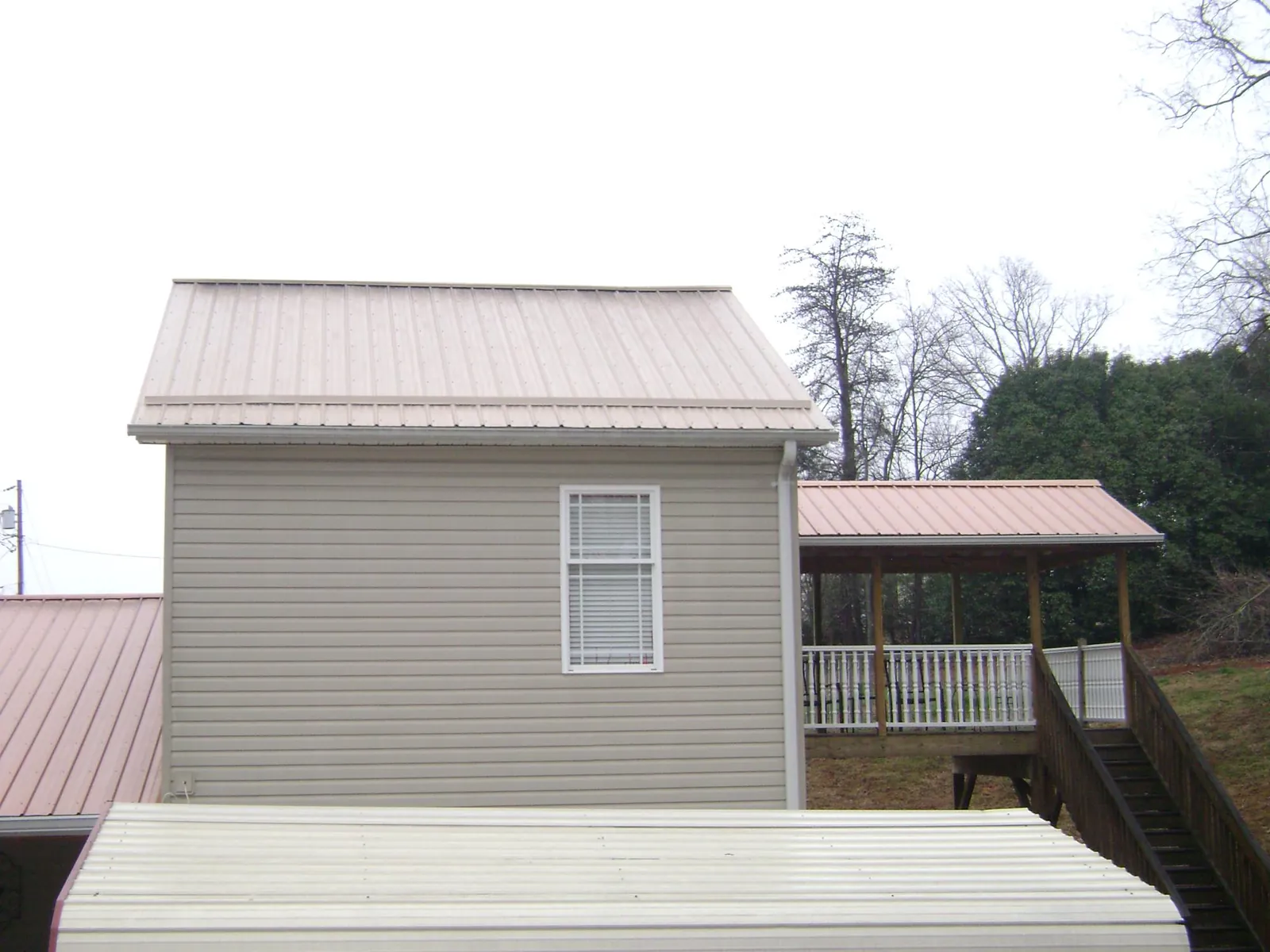 Tan metal roofs on a two story addition and attached porch, from a Roof Replacement job in Johnson